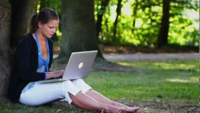 Still from the ad: a young woman with a laptop, sitting under a tree